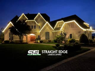 Elegant home adorned with soft white lights at night, showcasing professional landscaping.